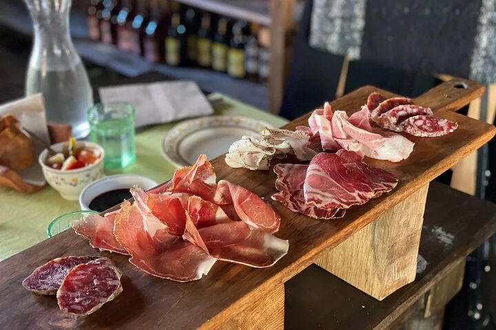 A wooden board of sliced cured ham and salami on a restaurant table with a carafe and small dishes