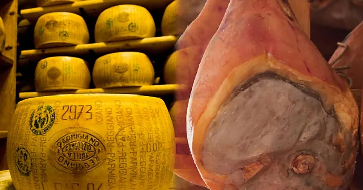Laibe Parmigiano Reggiano, in Regalen gestapelt neben einem luftgetrockneten Schinken