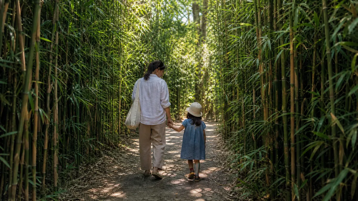 Ein Elternteil und ein Kind auf einem sonnigen Weg zwischen hohen Wänden aus grünem Bambus